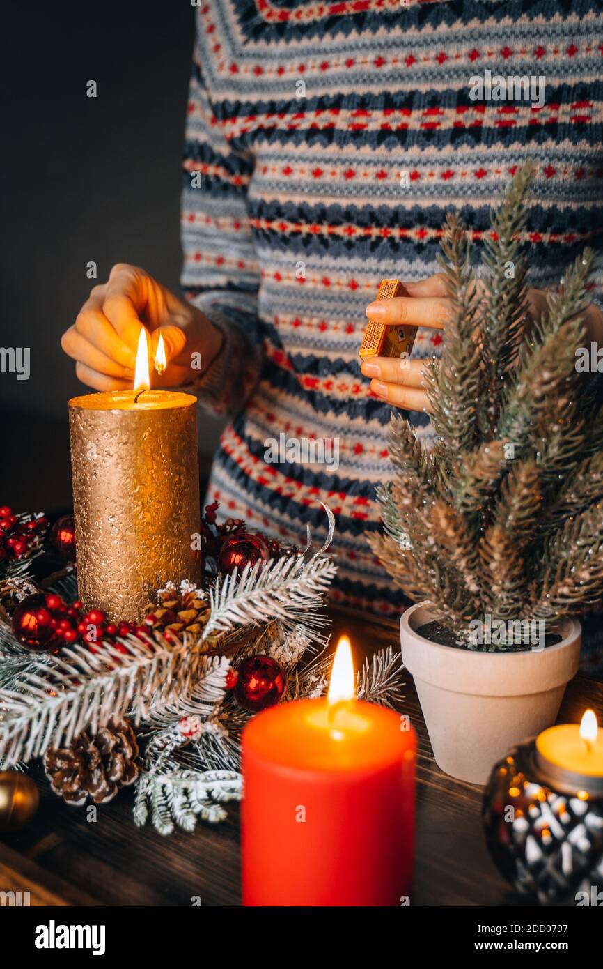 Weibliche Hand zündet Kerzen auf dekorierten Tisch zu Weihnachten. Neujahr  brennende Kerze, Adventszeit, warme Lichter, Winterdekorationen Ornamente  auf alten r Stockfotografie - Alamy