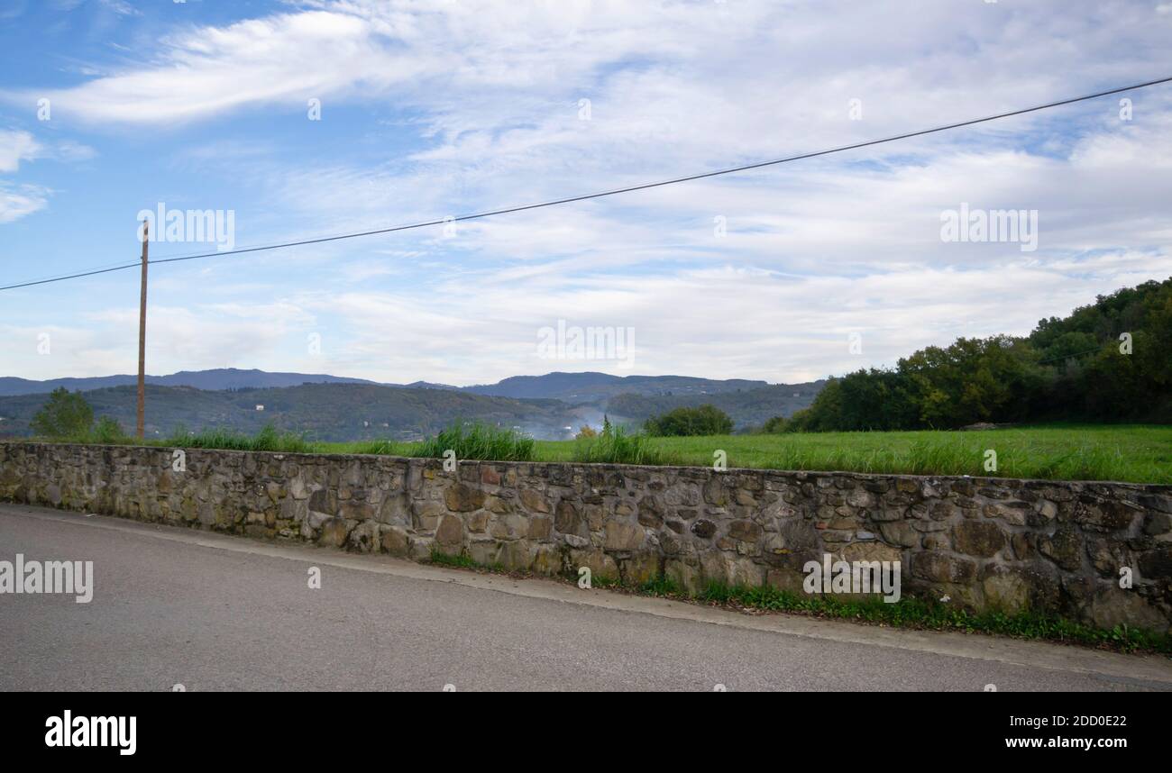 Lange perspektivische Ansicht einer Steinmauer entlang einer Landstraße mit bewölktem Himmel, in der Toskana Stockfoto