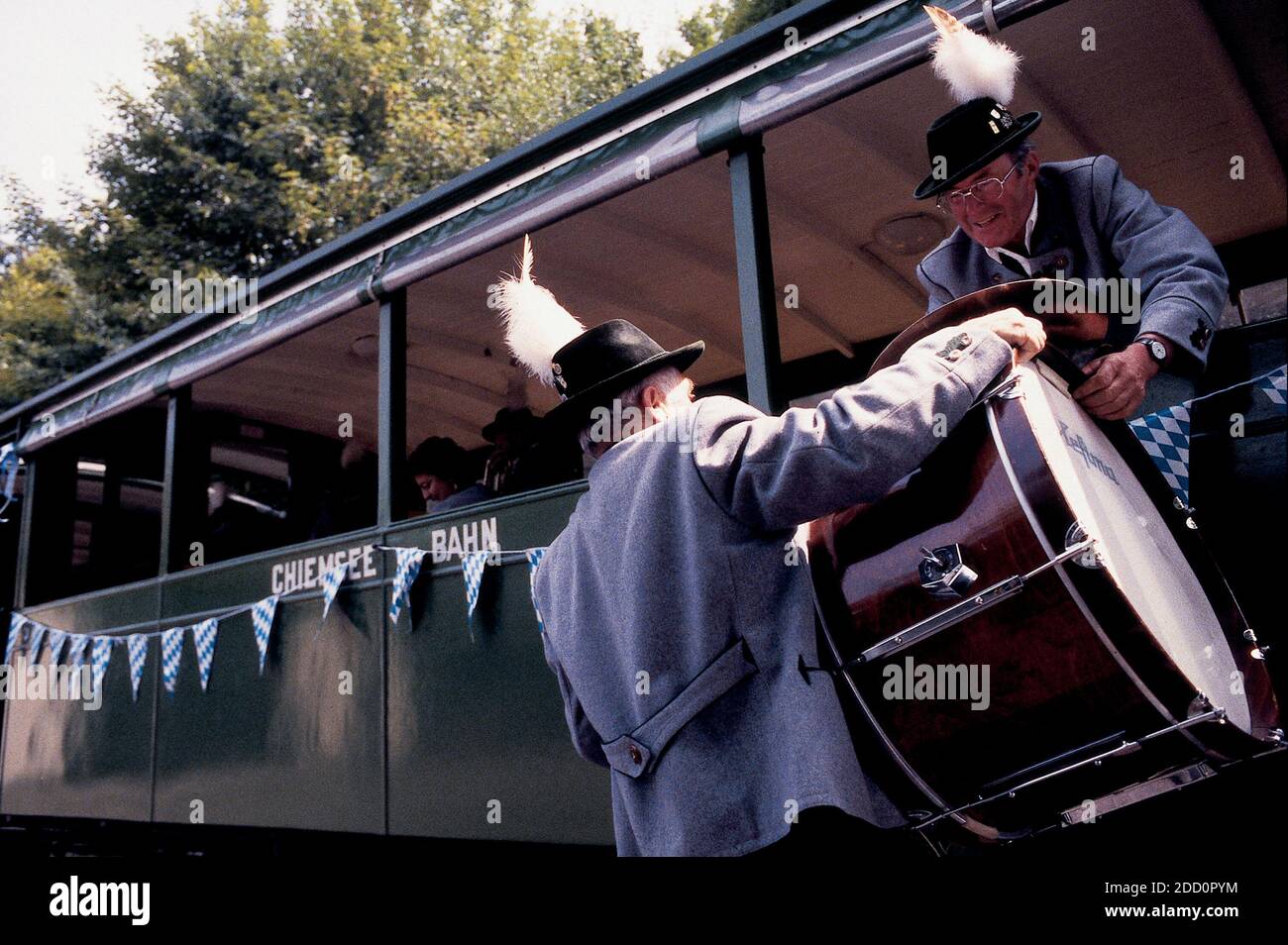 DEUTSCHLAND / Bayern / Chiemsee / Mann in traditioneller Kleidung unterwegs im Zug und sein Freund trägt dazu bei, seine große Trommel durch das Fenster zu laden. Stockfoto