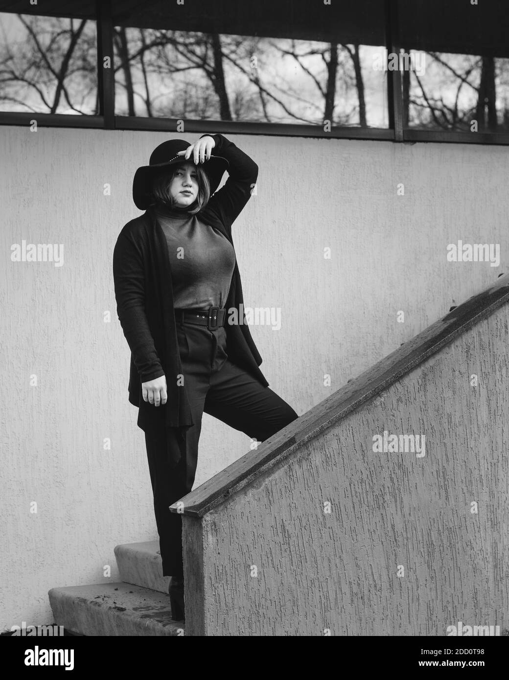 Brunette Frau im Hut auf der Treppe des Gebäudes in der Stadt. Plus-Modell. Schwarz und Weiß Stockfoto