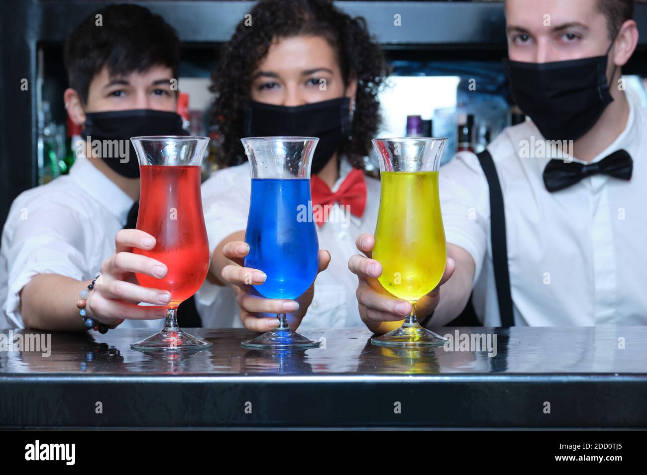 Drei Kellner mit Schutzmaske und drei bunten Cocktails in einer Kneipe. Neue Normalität in Pubs. Stockfoto
