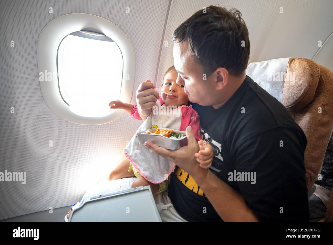 Vater füttert das kleine Kleinkind im Flugzeug mit speziellen Mahlzeiten. Stockfoto