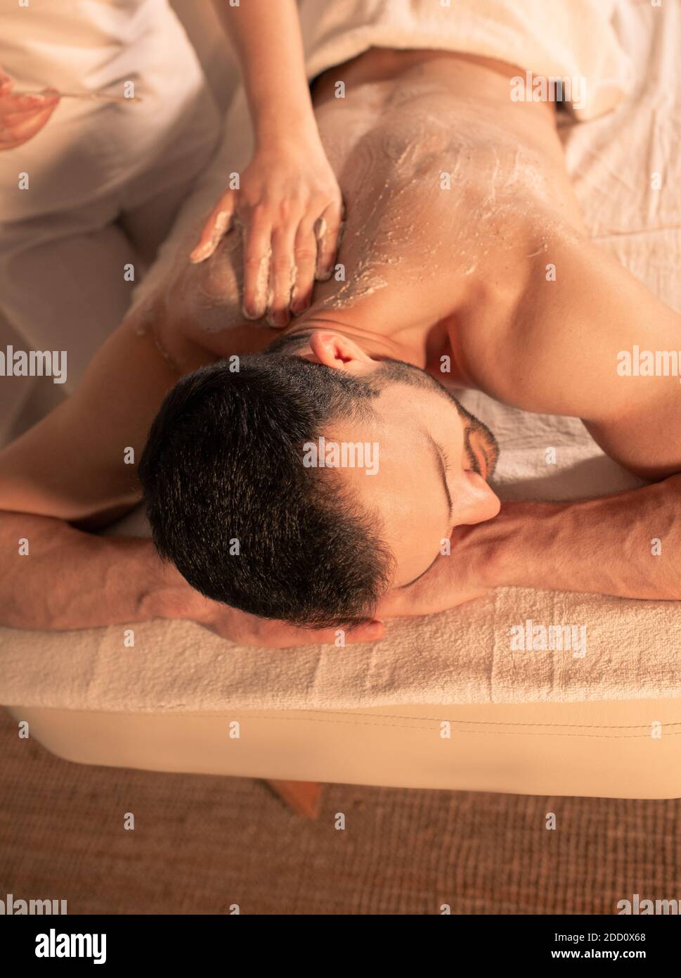 Gemischter Rennmensch erhält Körperpeeling mit Peeling im Spa-Salon. Draufsicht Stockfoto