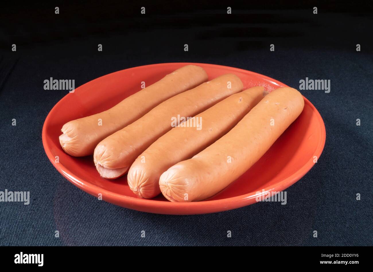 Die Hot Dogs auf dem Tisch in roter Platte auf schwarzem Hintergrund. Die Produkte der Fleischfütterung. Stockfoto
