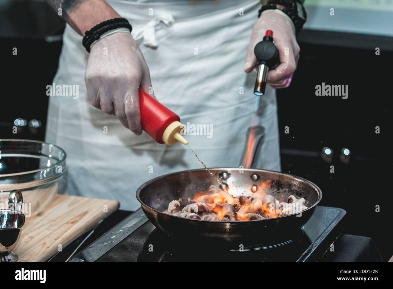 Der Koch kocht kleine Tintenfische auf einer Metallpfanne im Restaurant, um  brasilianisches Gericht zu machen. Pfanne brennt Stockfotografie - Alamy