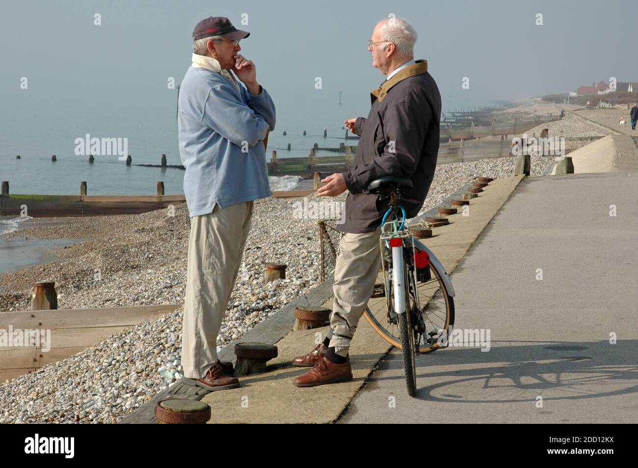 Zwei Männer, mittleren Alters bis ältere, stehen auf Küstenweg, um eine Diskussion zu führen. East Wittering, West Sussex. Stockfoto