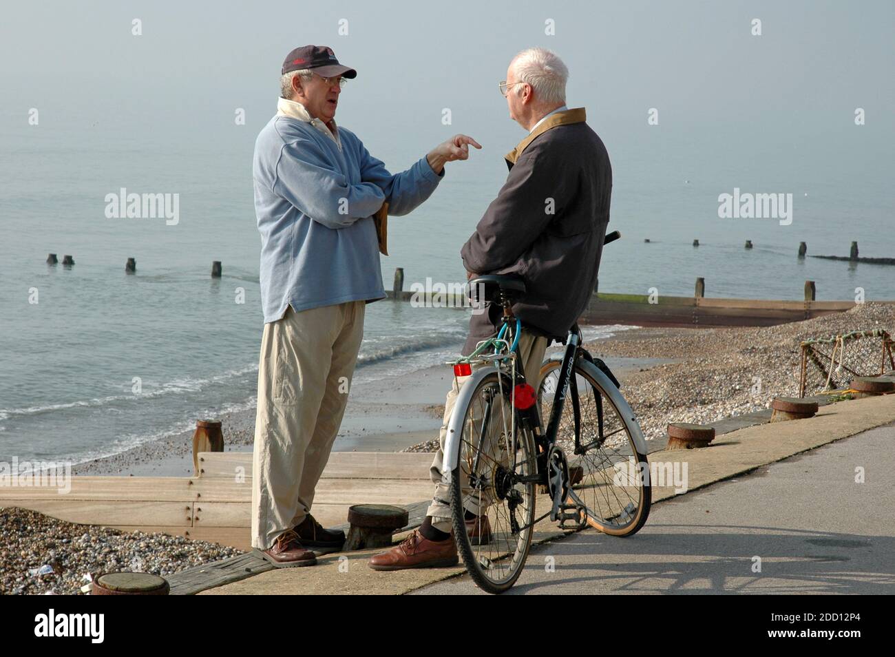 Zwei Männer, mittleren Alters bis ältere, stehen auf Küstenweg, um eine Diskussion zu führen. East Wittering, West Sussex. Stockfoto