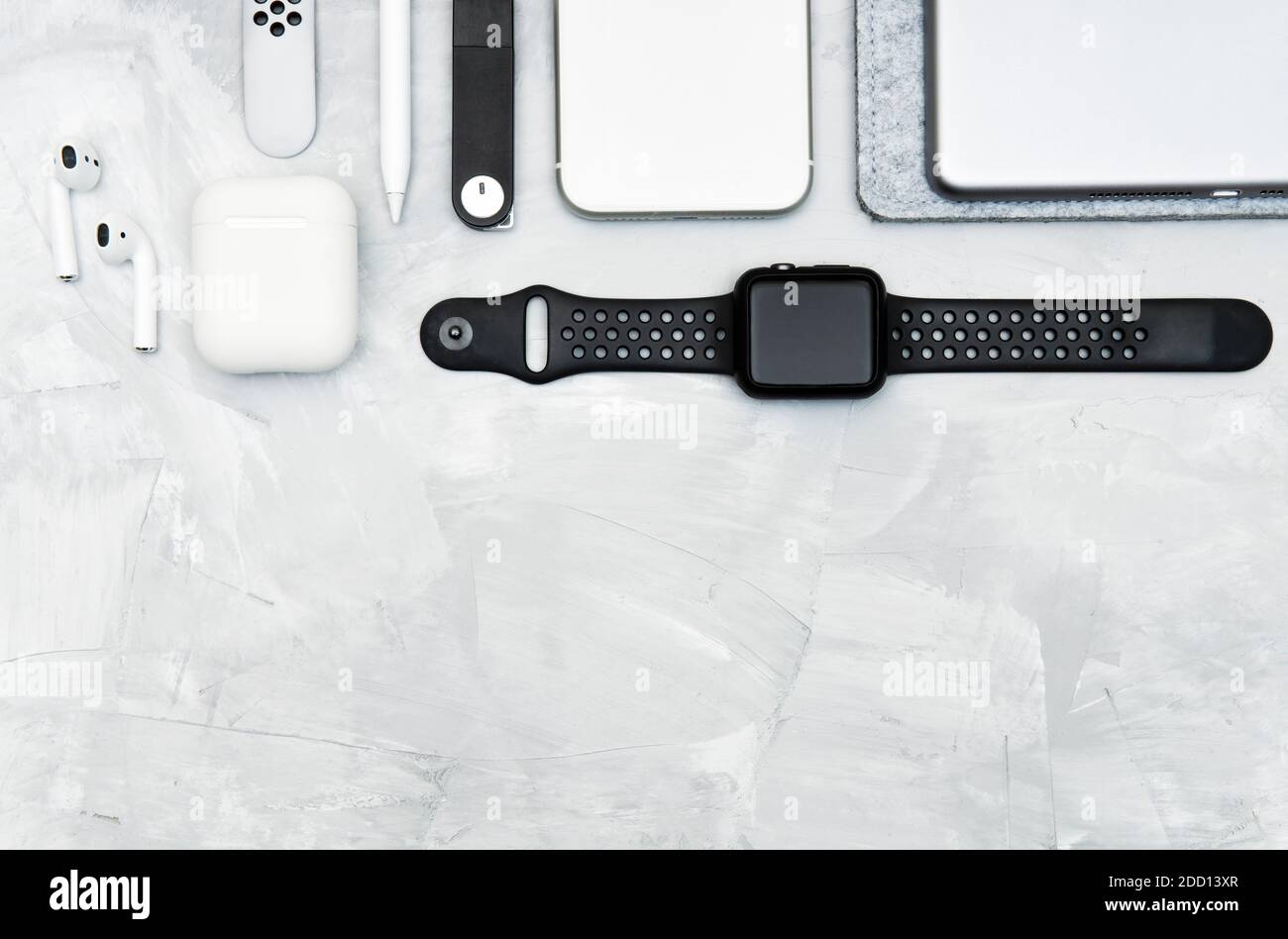 Moderne Alltagsgeräte tragen auf einem konkreten Schreibtisch: Smartphone, Smartwatch, digitales Tablet, Stylus Bleistift, kabellose Kopfhörer, Memory Stick. Schwarz und w Stockfoto