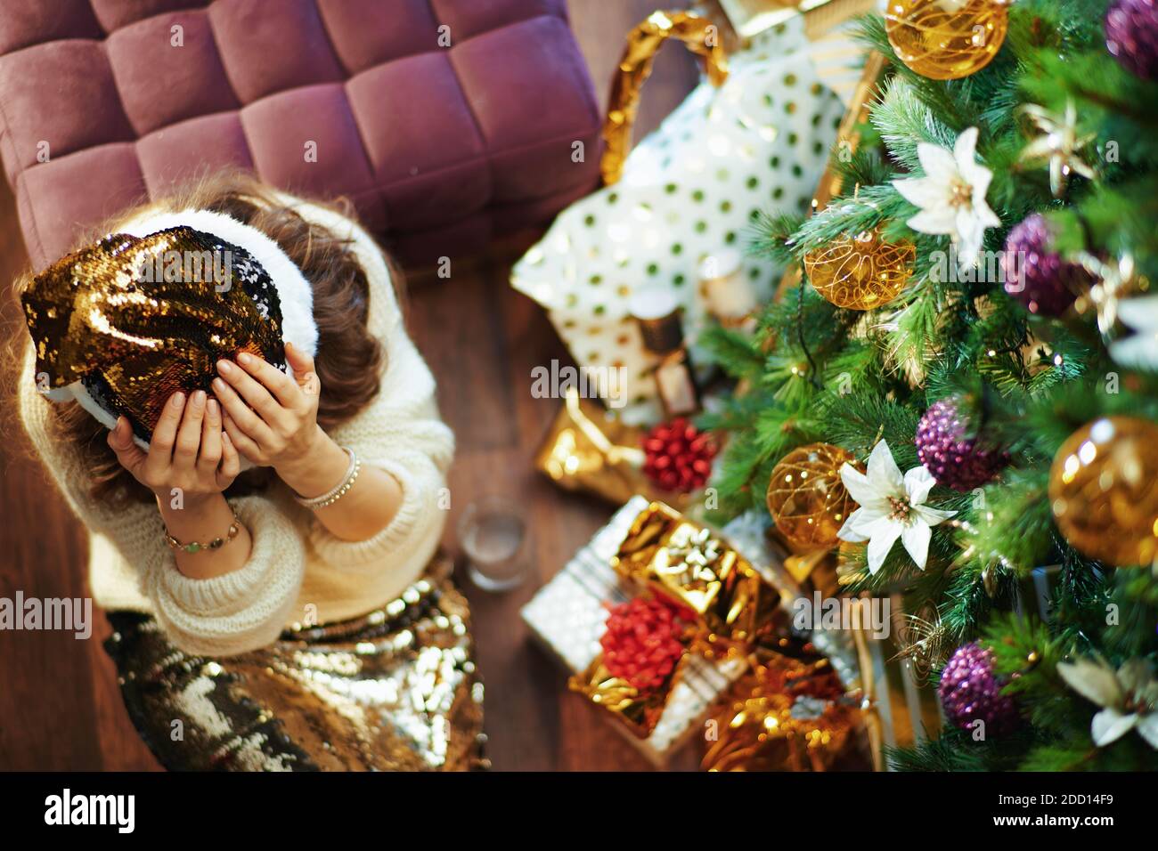 Frohe Weihnachten. Obere Ansicht der betont eleganten mittleren Alters Hausfrau in Gold Pailletten Rock und Pullover in der Nähe Weihnachtsbaum und Geschenkboxen. Stockfoto