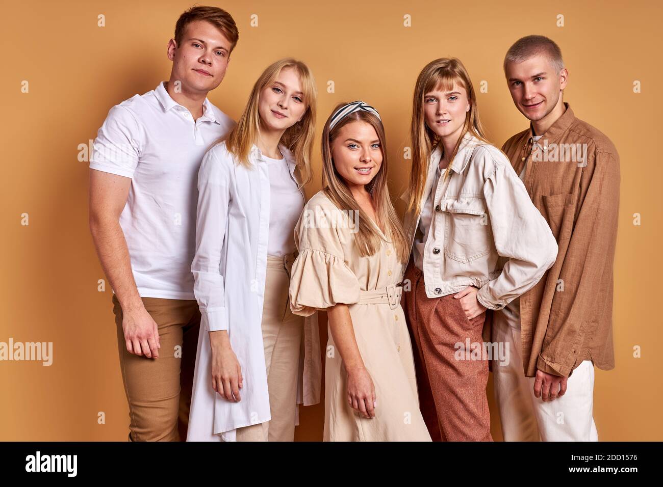 Portrait von trendy stilvolle Jugend posiert bei der Kamera isoliert auf braunem Hintergrund, gutaussehende männliche und schöne Frauen in modischen braunen Kleidung stehen zusammen, Modelle Stockfoto