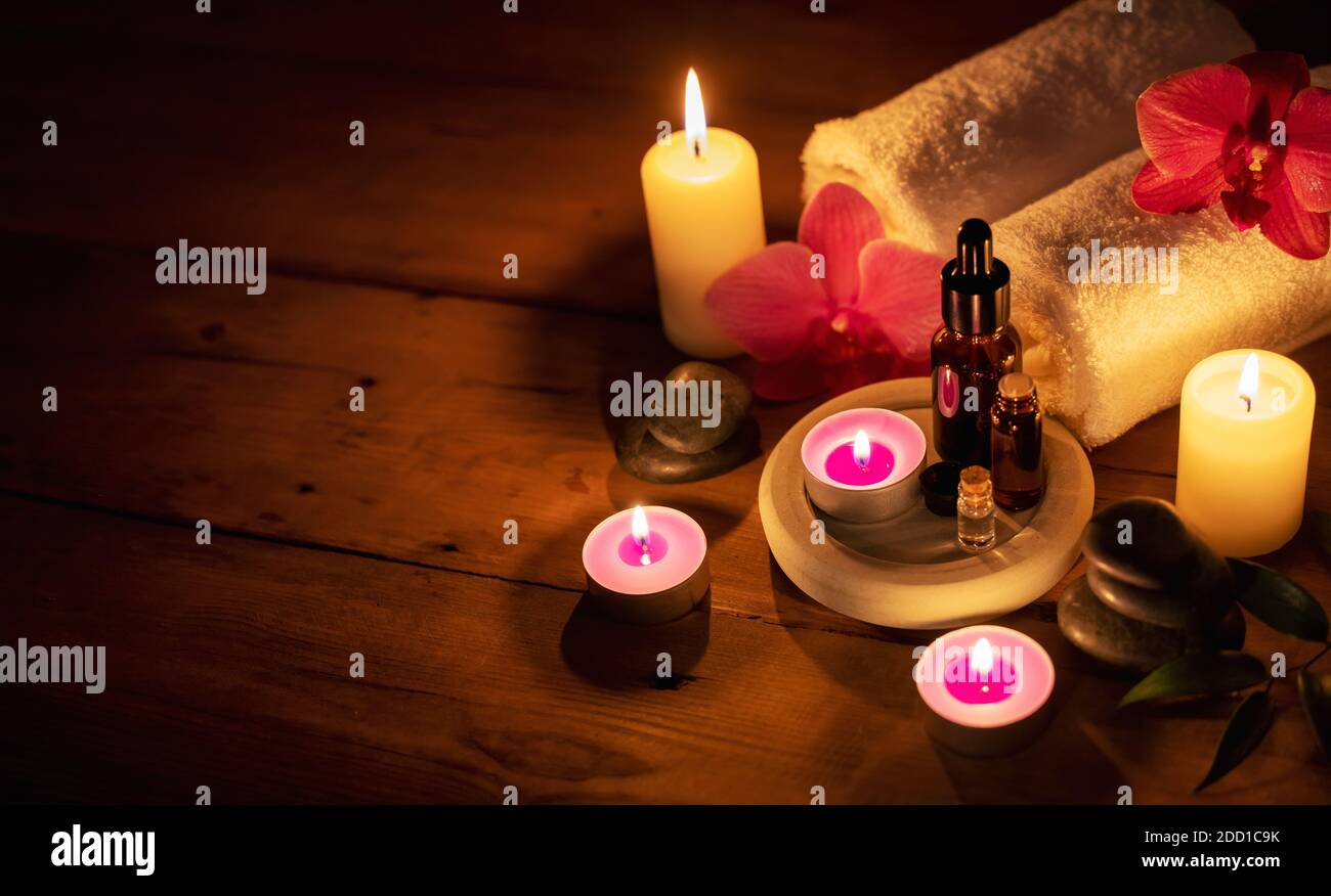 Romantisches Spa - ätherische Öle mit Massagesteinen und Blumen Im Cadlelight auf Holzhintergrund mit Kopierraum Stockfoto