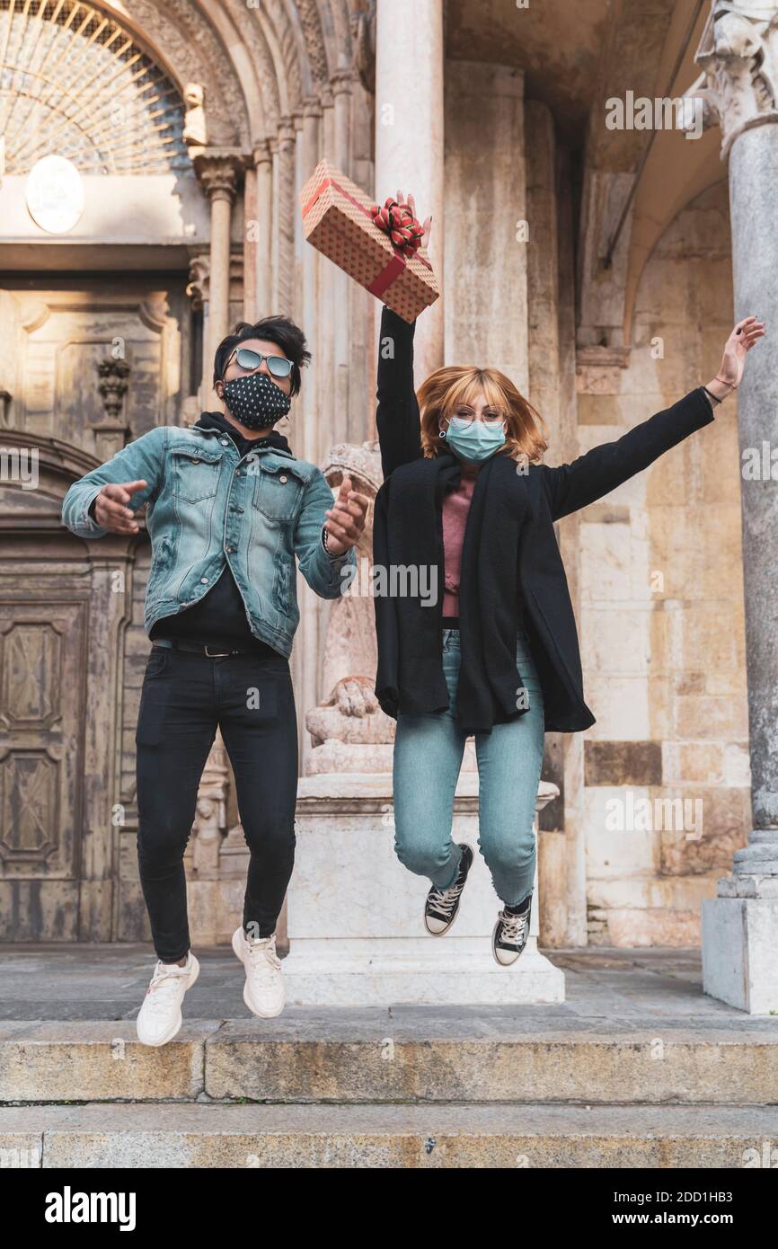 Junge glücklich Paar trägt Maske in der Zeit der Coronavirus springen Mit einem Geschenk in der Hand Stockfoto