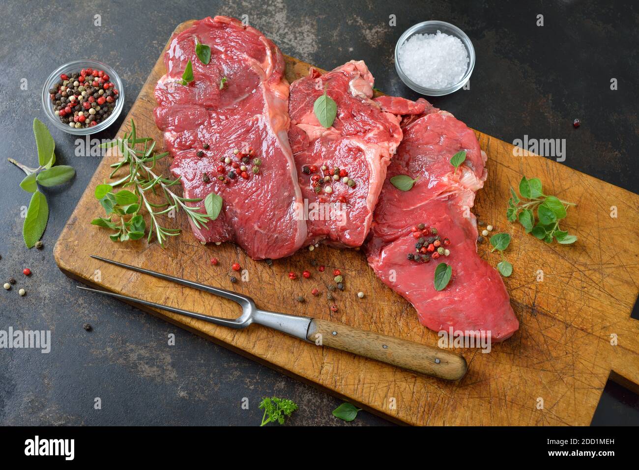 Drei rohe Rib Eye Steaks mit Gewürzen und Kräutern auf Ein altes Holzschneidebrett Stockfoto
