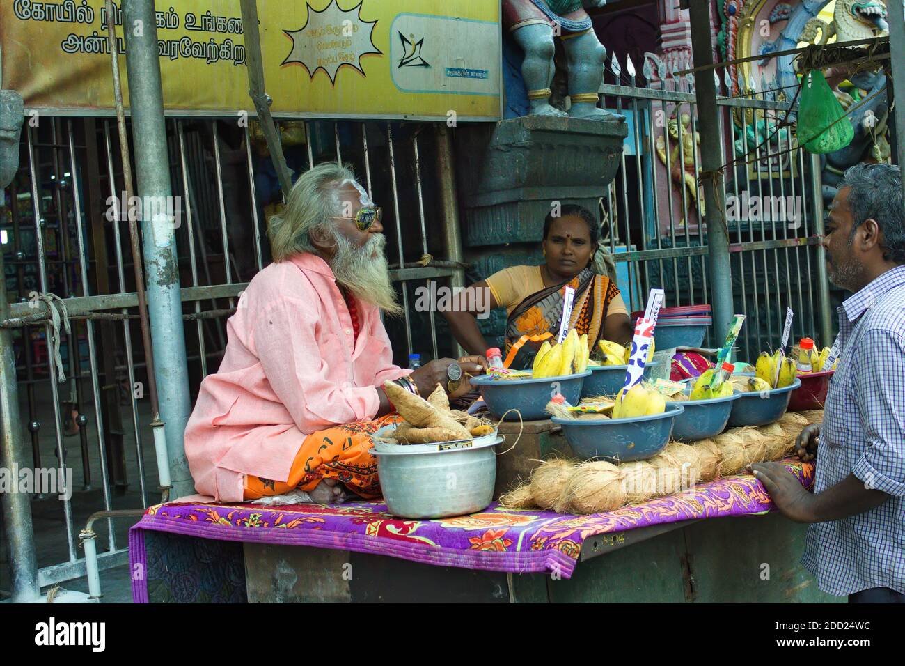 Madurai, Indien - 02. November 2018: Ein alter Sadhu-Mann, der Kokosnuss und Früchte zu Gebetszwecken vor einem hindu-Tempel namens Thiruparankundra verkauft Stockfoto