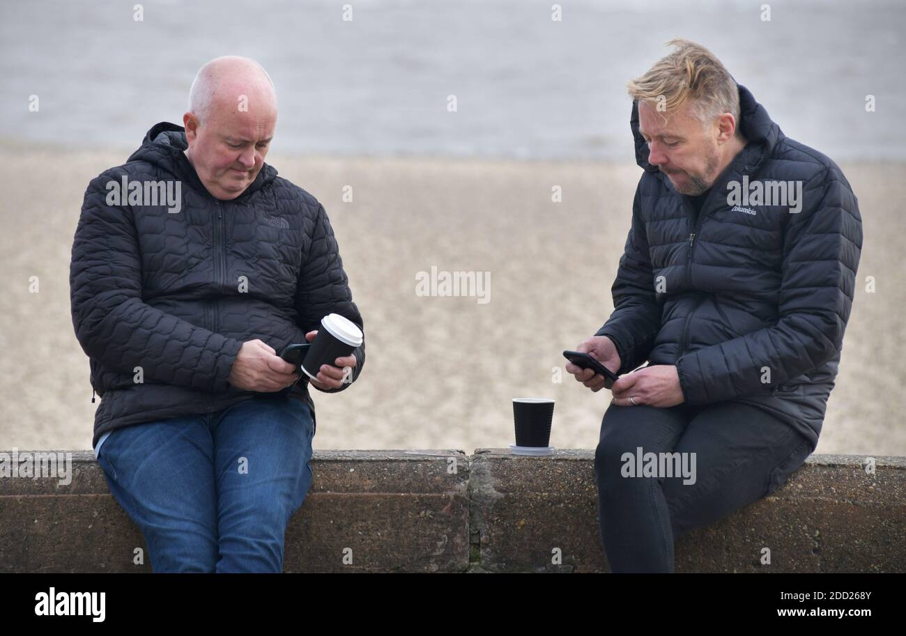 Männer mittleren Alters mit Kaffeetassen, die auf das Handy schauen Bildschirme Stockfoto