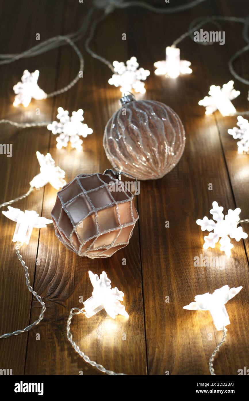 Rosa und weiße Weihnachtskugeln liegen zusammen mit einer leuchtenden Girlande auf einem braunen Holztisch. Nahaufnahme Stockfoto