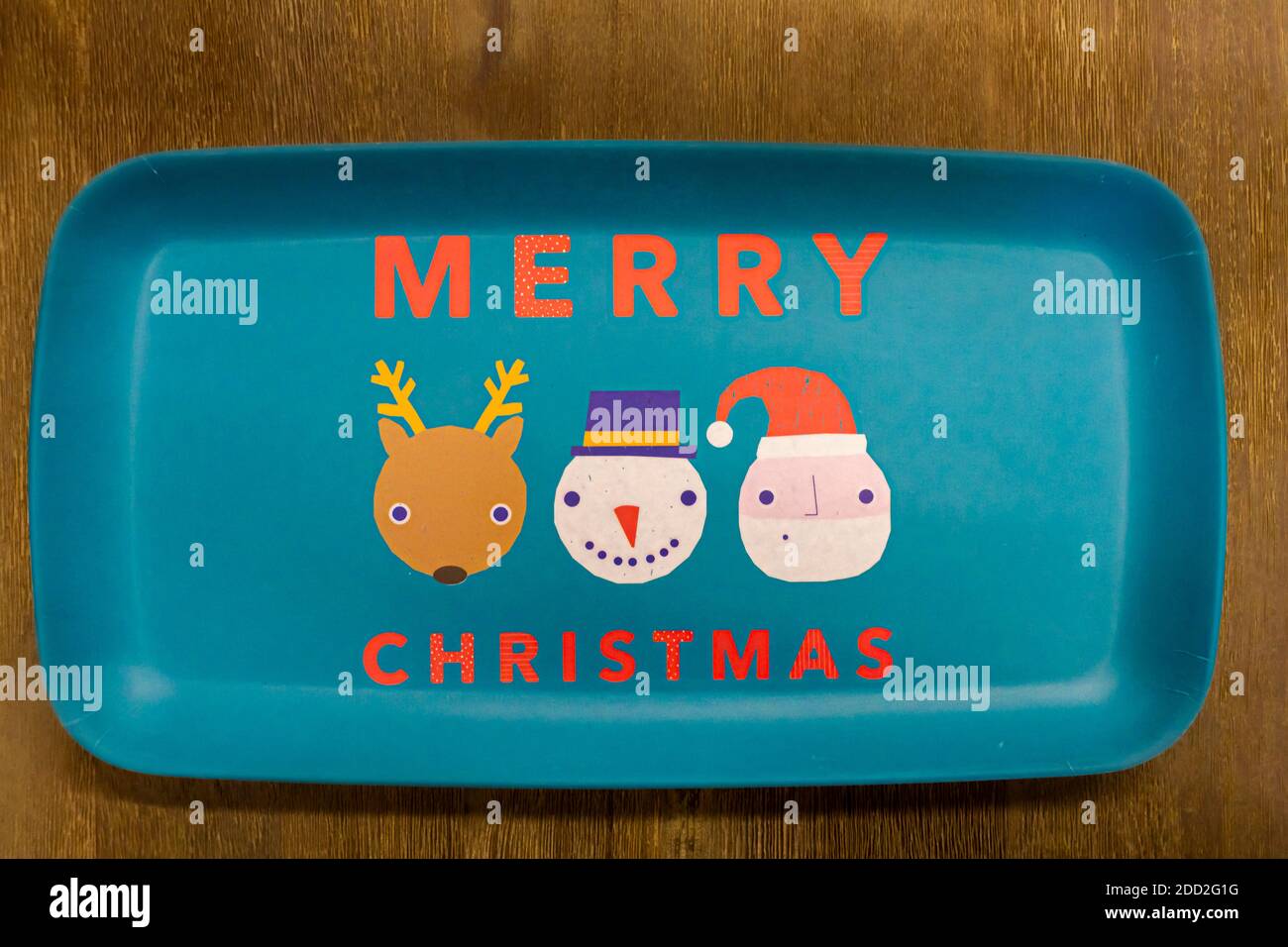 Flache Lay Bild einer turqoise recttengular Melamin Platte mit einem Reh Zügelwild, Schneemann und weihnachtsmann Figuren darauf. Die Platte auf Holztisch hat einen Text Stockfoto