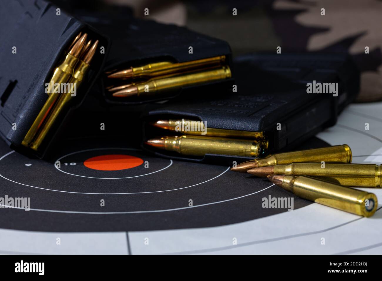 Geladene Gewehrmagazine mit losen Munition, die auf einem Papierziel mit Tarnhintergrund verstreut sind. Hintergrund- und Vordergrundunschärfe Stockfoto