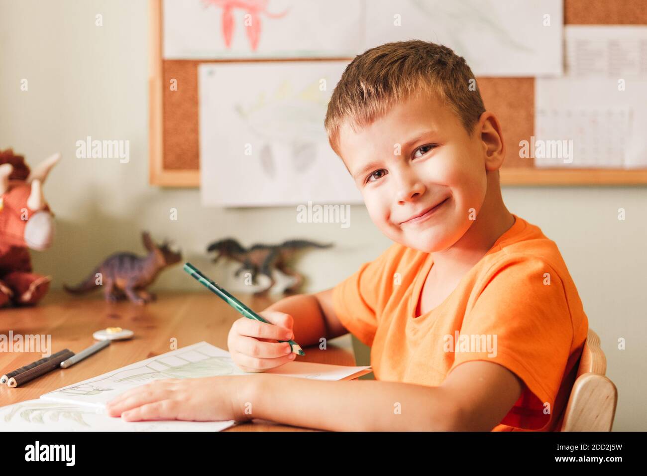 Nettes Kind Junge Zeichnung Dinosaurier auf Bild mit Buntstiften Sitzen am Schreibtisch in seinem Zimmer Stockfoto