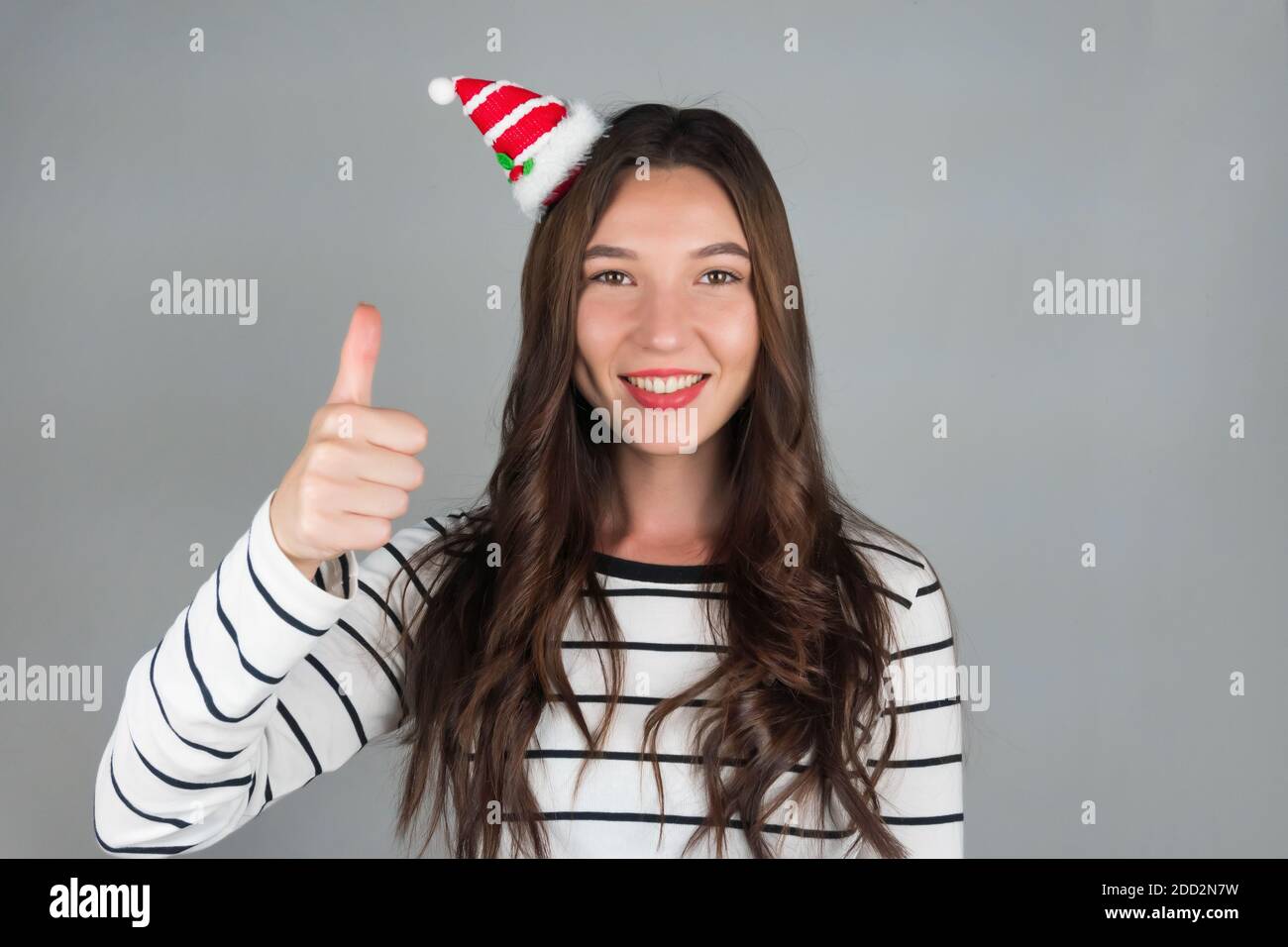 Ein junges Mädchen mit weihnachtlicher Dekoration im Haar posiert für ein Auto. Halten Sie Ihre Finger oben, positive Emotionen. Hochwertige Fotos Stockfoto