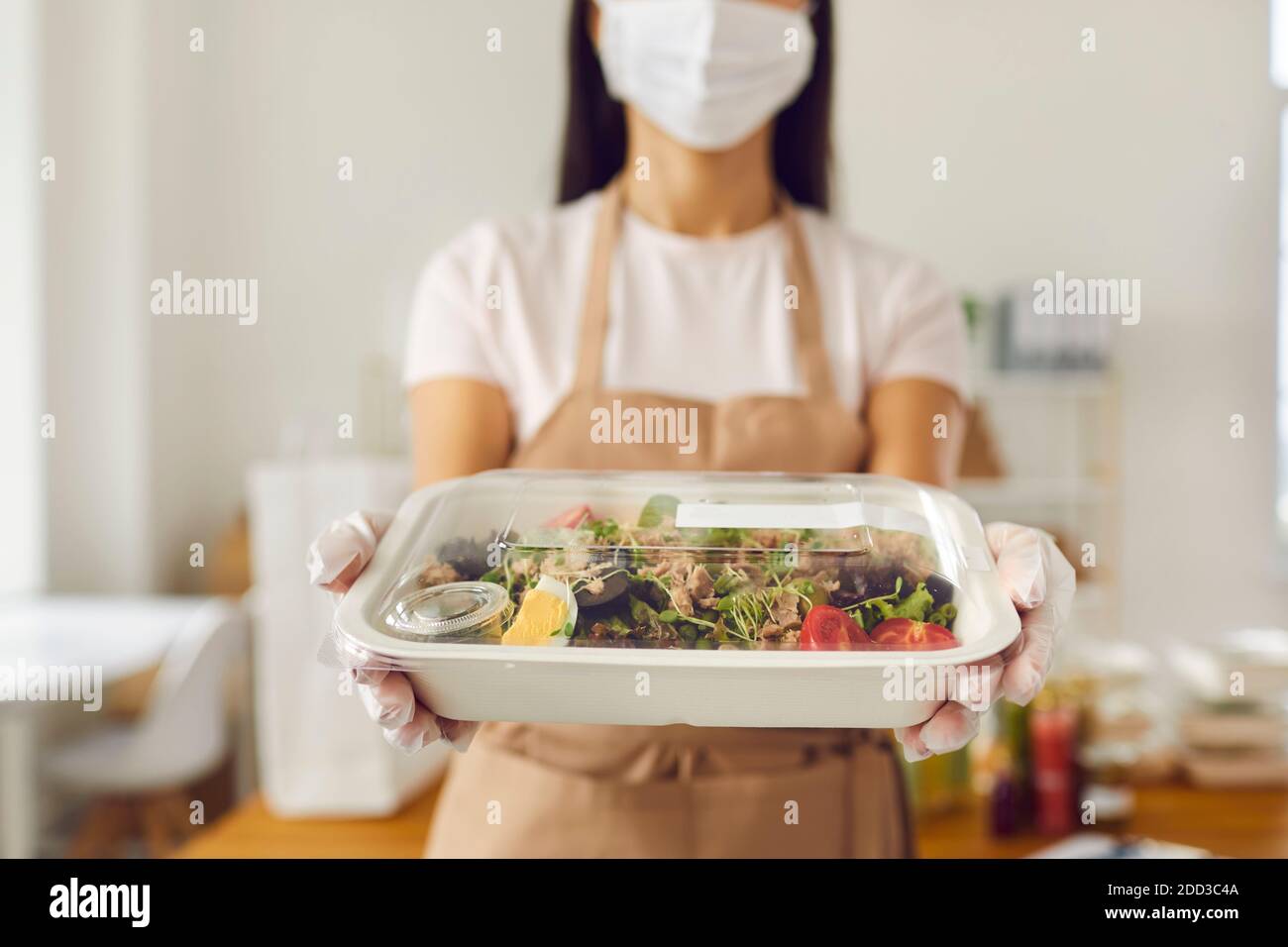 Verantwortungsbewusster Mitarbeiter im Café zum Mitnehmen in der Gesichtsmaske, der das Lunchpaket hält Bereit zur Lieferung Stockfoto