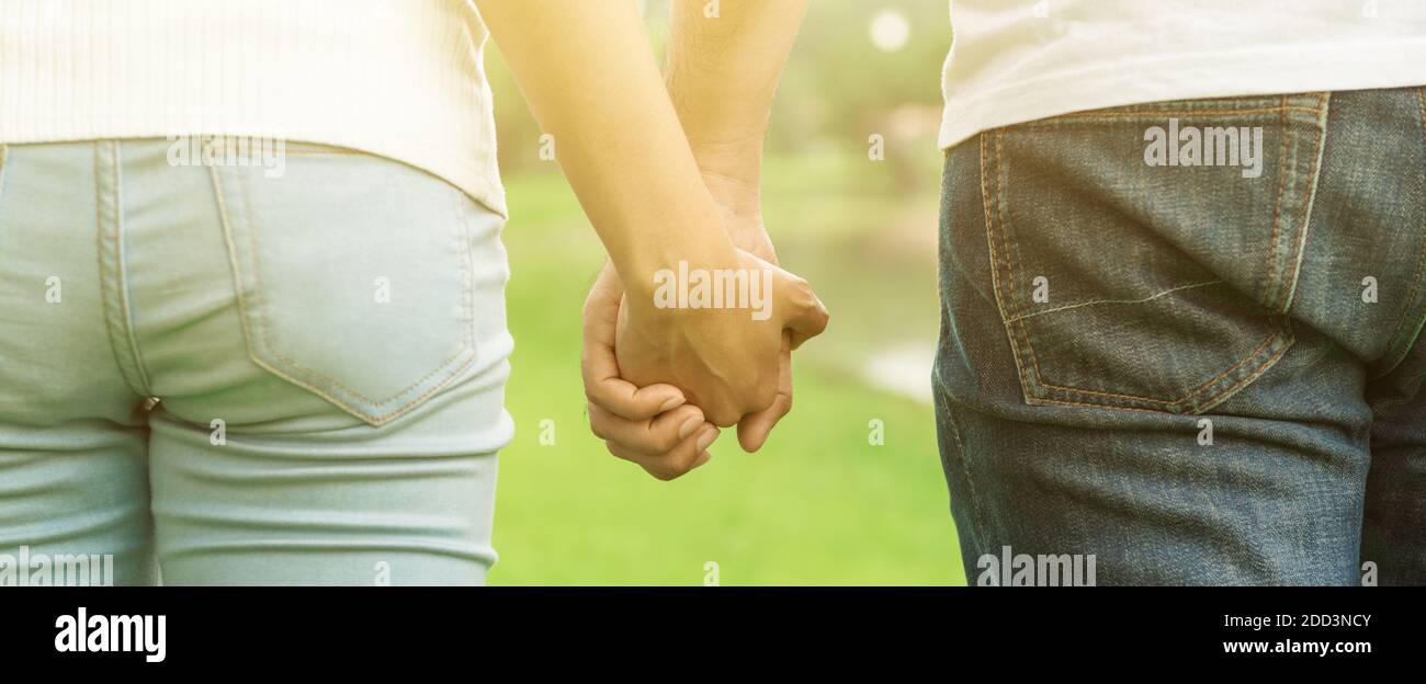 Rückansicht eines jungen, zwanglosen Paares, das beim Spaziergang im Park die Hände hält - Dating, Liebesgedanken und Liebesgedanken Stockfoto