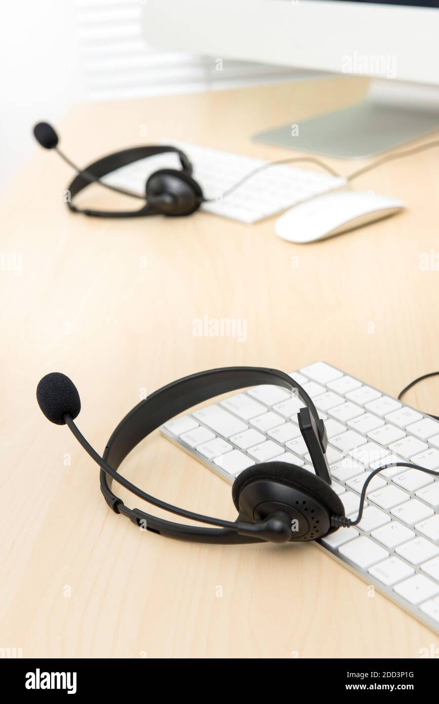 Mikrofon-Headsets auf dem Tisch mit Computertastaturen im Callcenter, selektiver Fokus Stockfoto