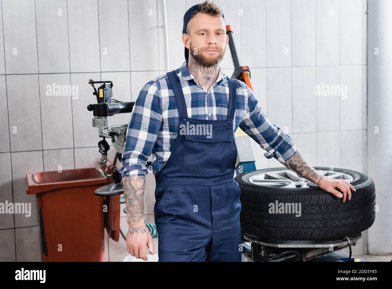 Junger Mechaniker im Overall, der beim Reifenwechsel in der Nähe des Rades  steht Maschine in Werkstatt Stockfotografie - Alamy