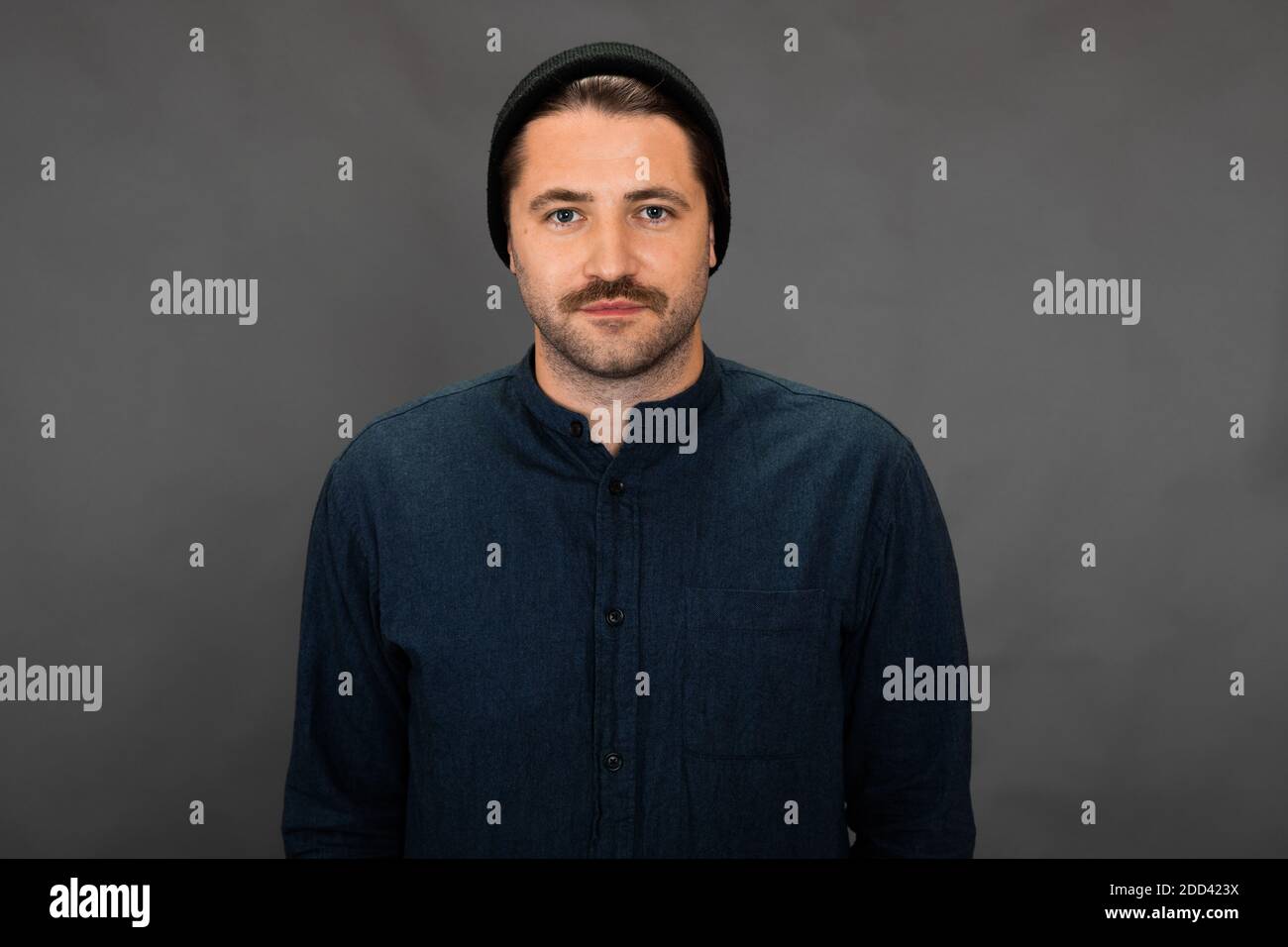 Schöner moustached unrasiert Kerl in gestrickten Mütze posiert auf grau studiohintergrund Stockfoto