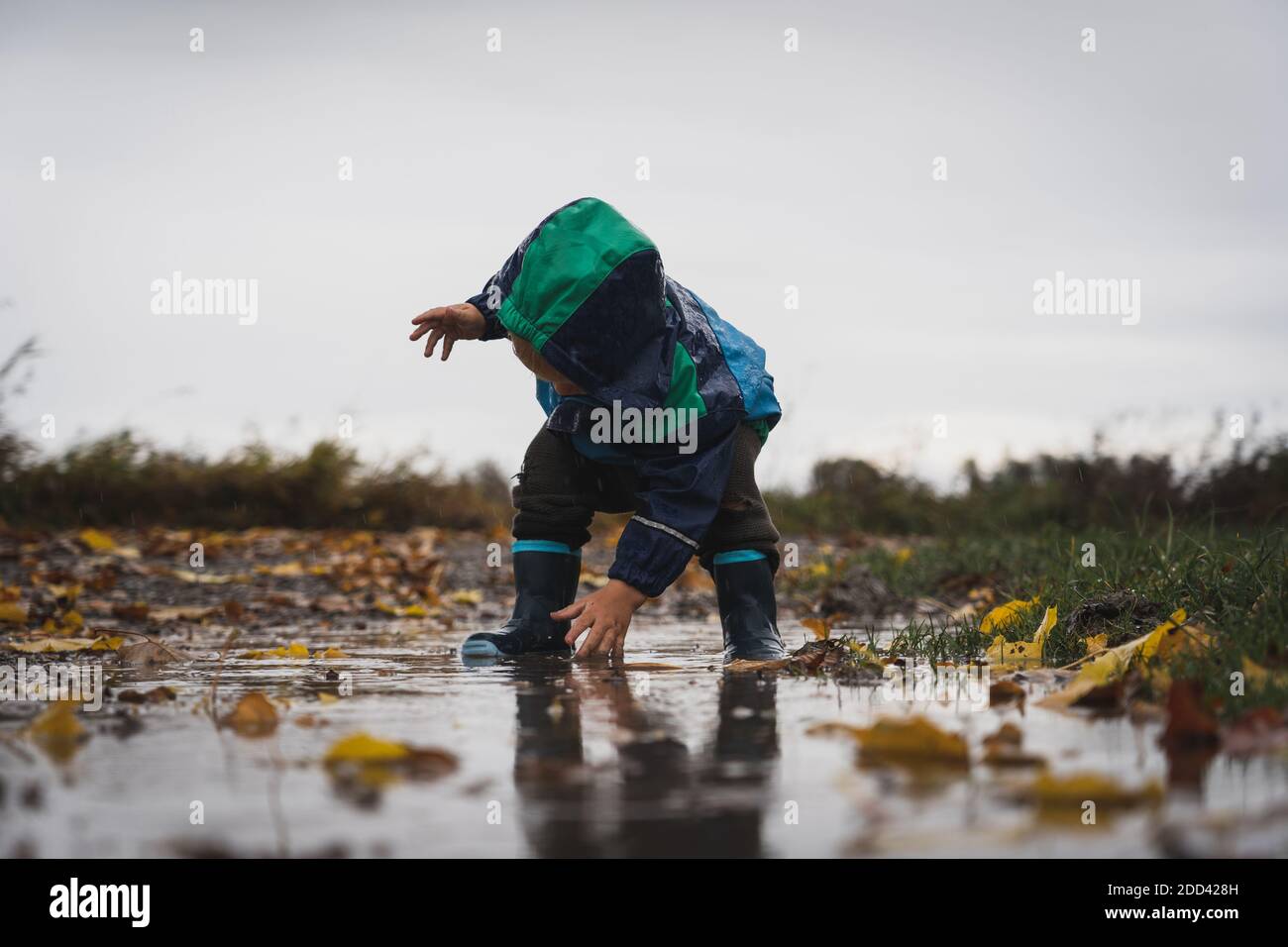 Ein kleiner Junge spielt in einer Pfütze im Regen. Glücklich glückselig keine Sorge in der Welt. Schön verspielt und berührend. Stockfoto