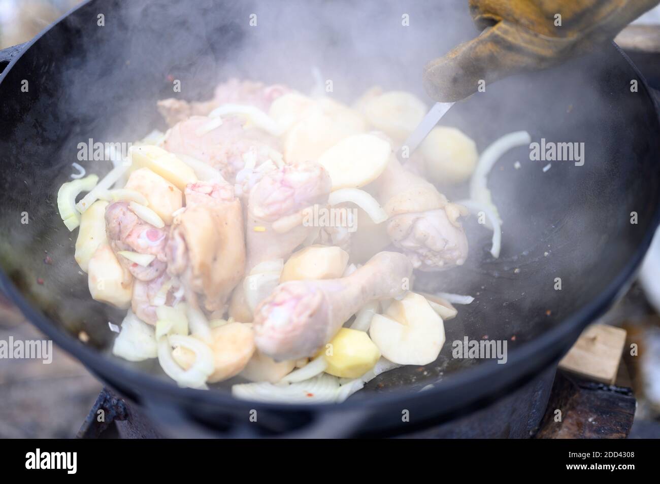 Entkoketes Foto vom Kochen im Winter in einem Kessel im Freien auf einem Feuer. Essen aus Kartoffeln, Zwiebeln und Hühnerfleisch wird in einem Gusseisen c zubereitet Stockfoto