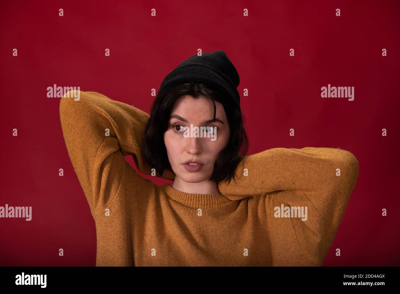 Brunette Hipster Mädchen in schwarz gestrickt Mütze und Senf Pullover Die Hände nach oben stellen Stockfoto