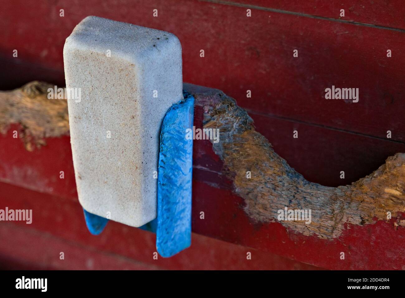 Ein gebrauchter Salzblock für Nutztiere hing an einer roten Scheunenwand. Stockfoto
