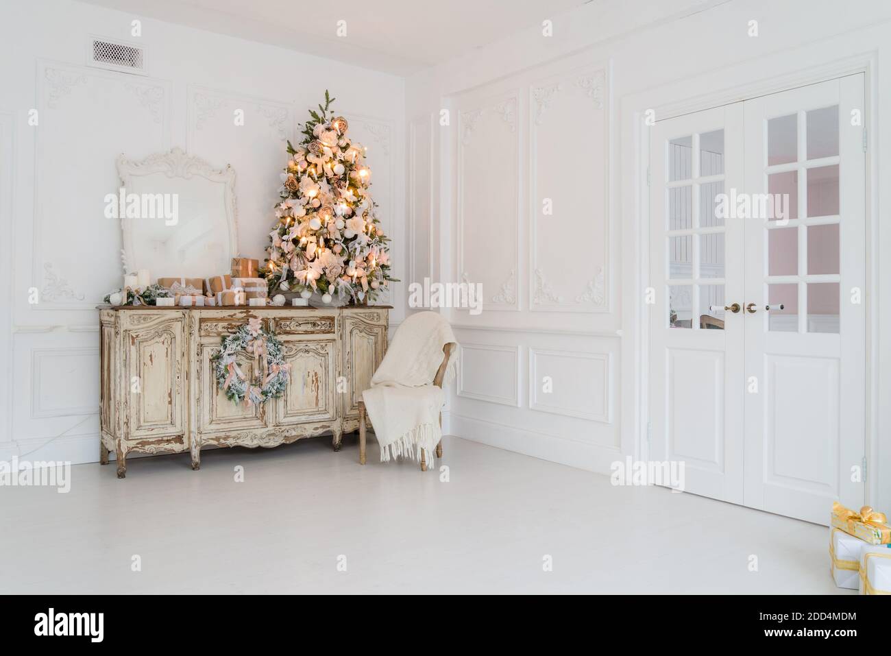 Geschmückter Weihnachtsbaum auf hölzerne Kommode Kommode Kommode in weiße Interieur mit künstlichen Blumen, Girlanden und Spielzeug Stockfoto