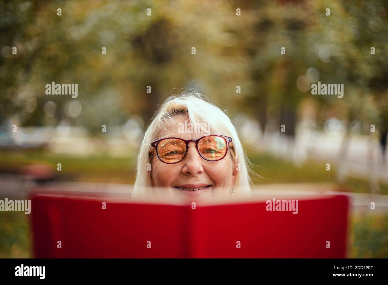 Nahaufnahme einer Frau in der Brille liest ein Red Book beim Entspannen im Park Stockfoto