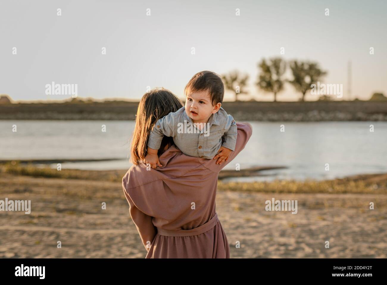 Portrait einer glücklichen, liebevollen Mutter, die ihren kleinen Sohn im sonnigen Park am Fluss umarmt. Stockfoto
