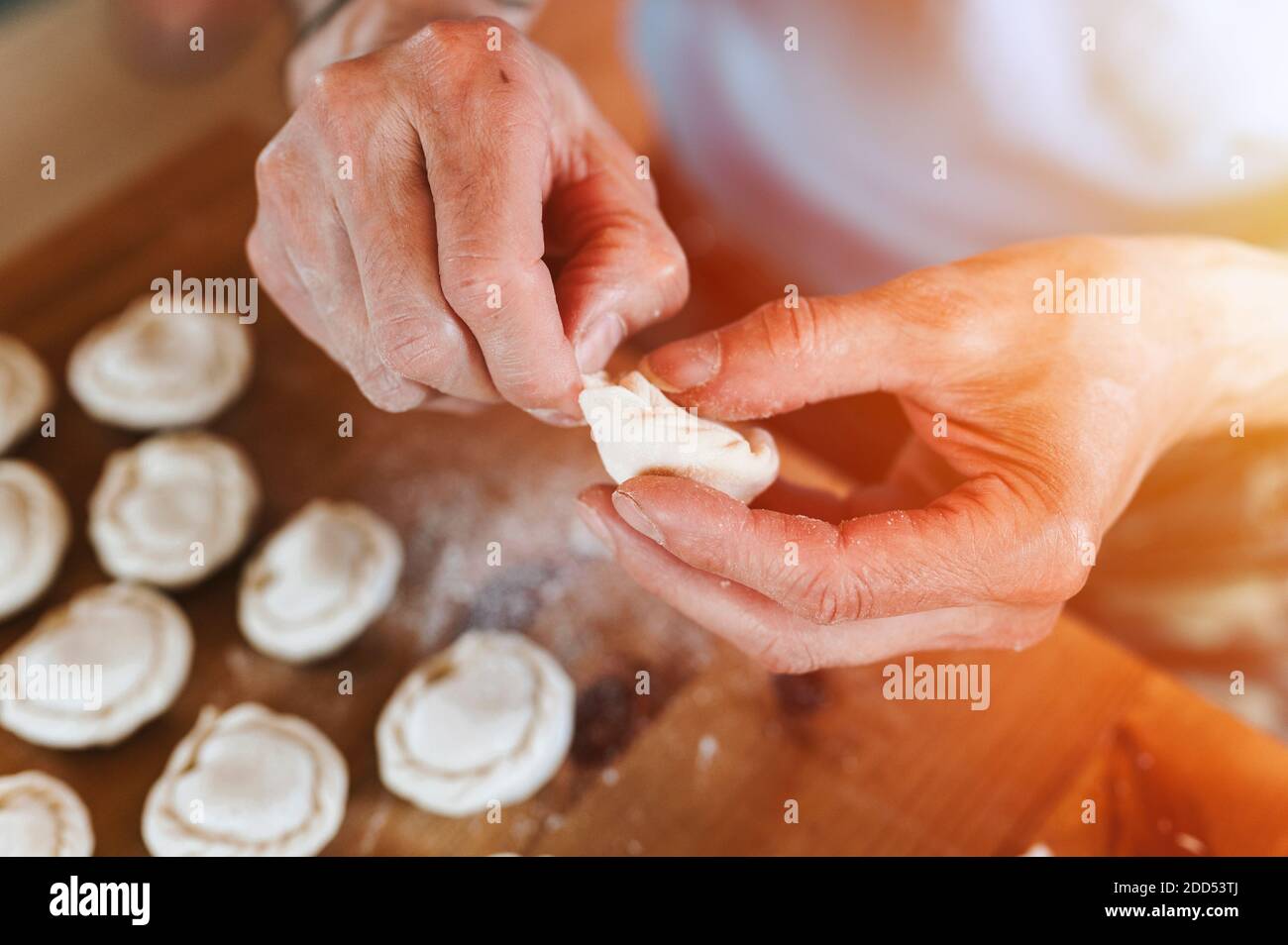 Hände von Senior Mann Kochen und Formen kleine hausgemachte ungekochte Knödel mit Fleisch auf Küchentisch. Nationale traditionelle russische Küche. Tun Sie es Ihre Stockfoto