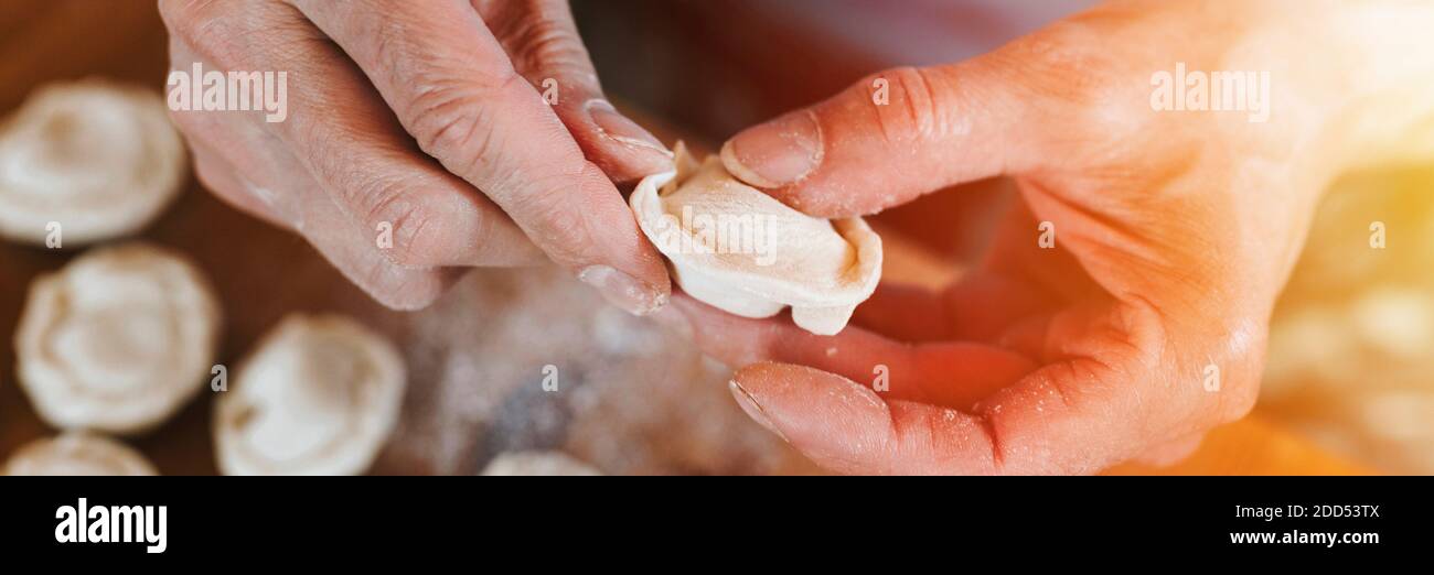 Hände von Senior Mann Kochen und Formen kleine hausgemachte ungekochte Knödel mit Fleisch auf Küchentisch. Nationale traditionelle russische Küche. Tun Sie es Ihre Stockfoto
