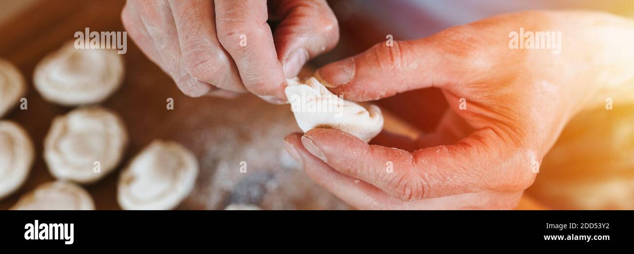 Hände von Senior Mann Kochen und Formen kleine hausgemachte ungekochte Knödel mit Fleisch auf Küchentisch. Nationale traditionelle russische Küche. Tun Sie es Ihre Stockfoto