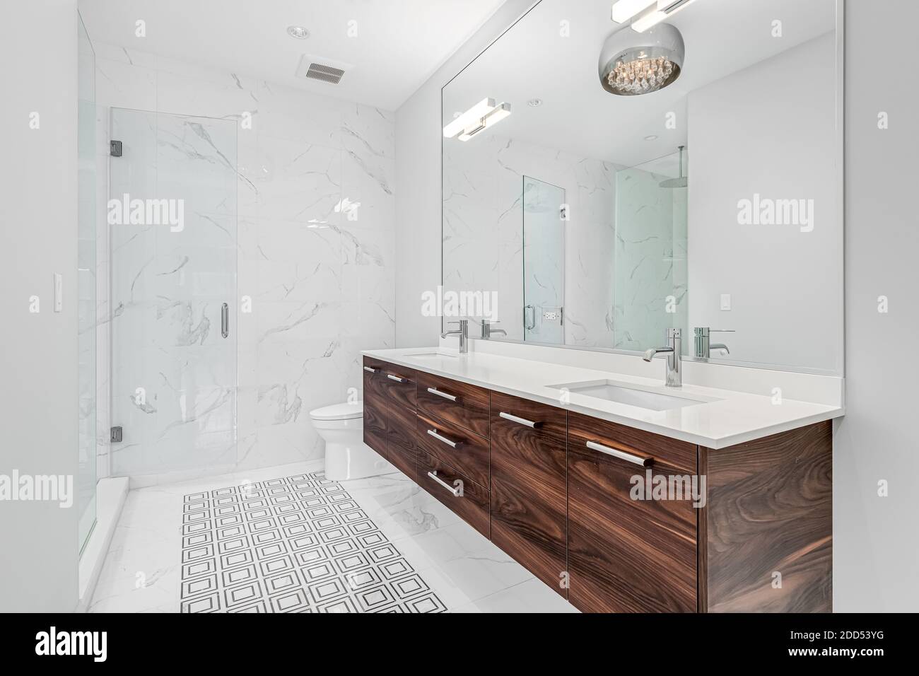 Ein großes, luxuriöses Badezimmer mit einem Holzwaschtisch, gemustertem Fliesenboden und Glas-Duschtüren. Stockfoto