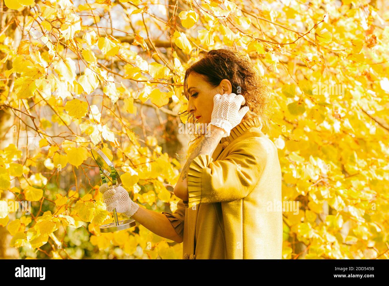 Frau retuschiert ihr Haar vor dem Spiegel inmitten eines gelblichen Parks, spanien Stockfoto