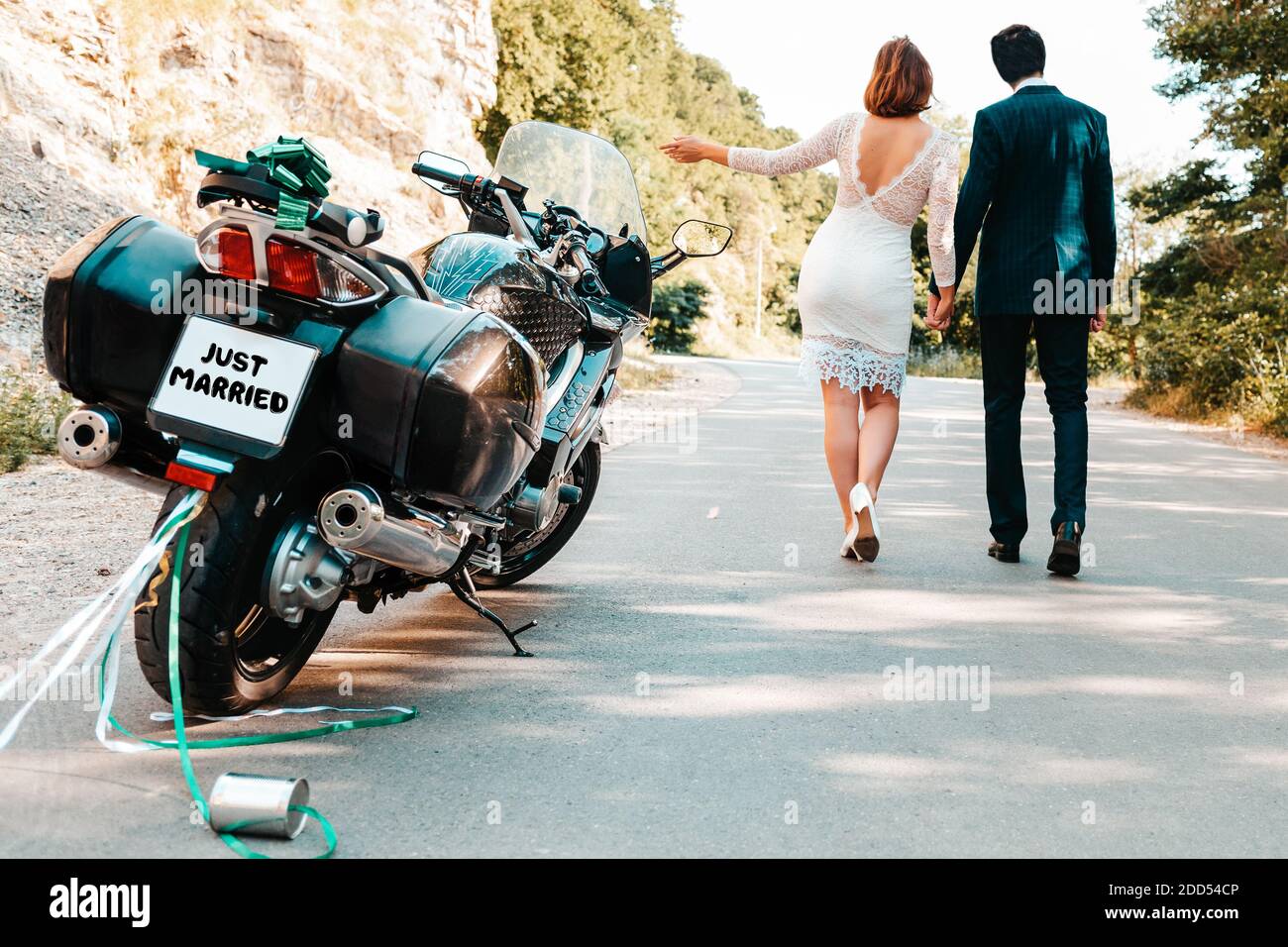 Hochzeit, frisch vermählt. Ein Mann und eine Frau in Hochzeitskleider  halten sich die Hände und gehen entlang der Straße. Ihr Motorrad ist auf  der Seite der Th geparkt Stockfotografie - Alamy