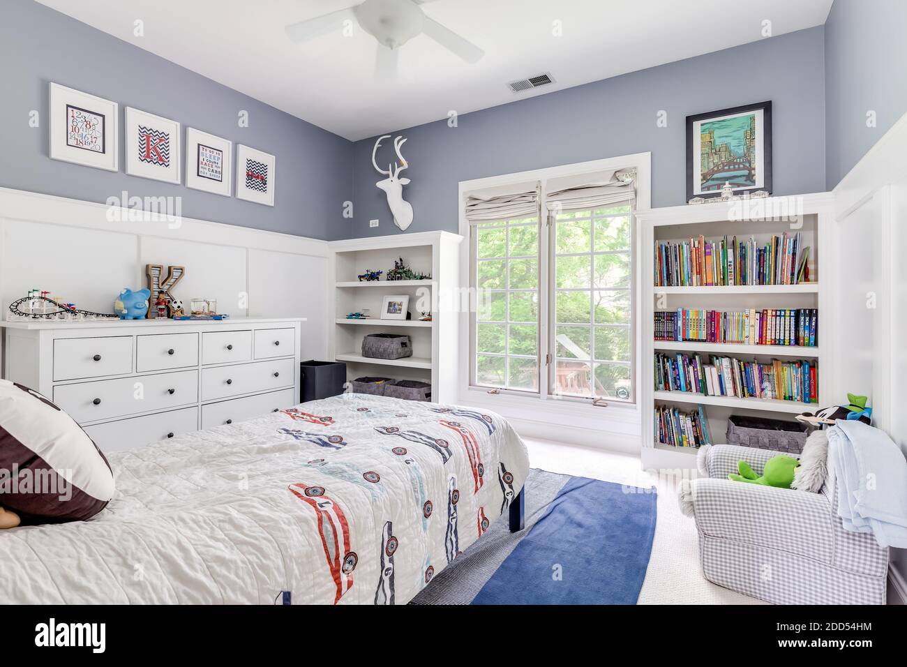 Ein gemütliches Schlafzimmer mit weißen und violetten Wänden, eingebauten Bücherregalen gefüllt mit Büchern und Kinderspielzeug. Stockfoto