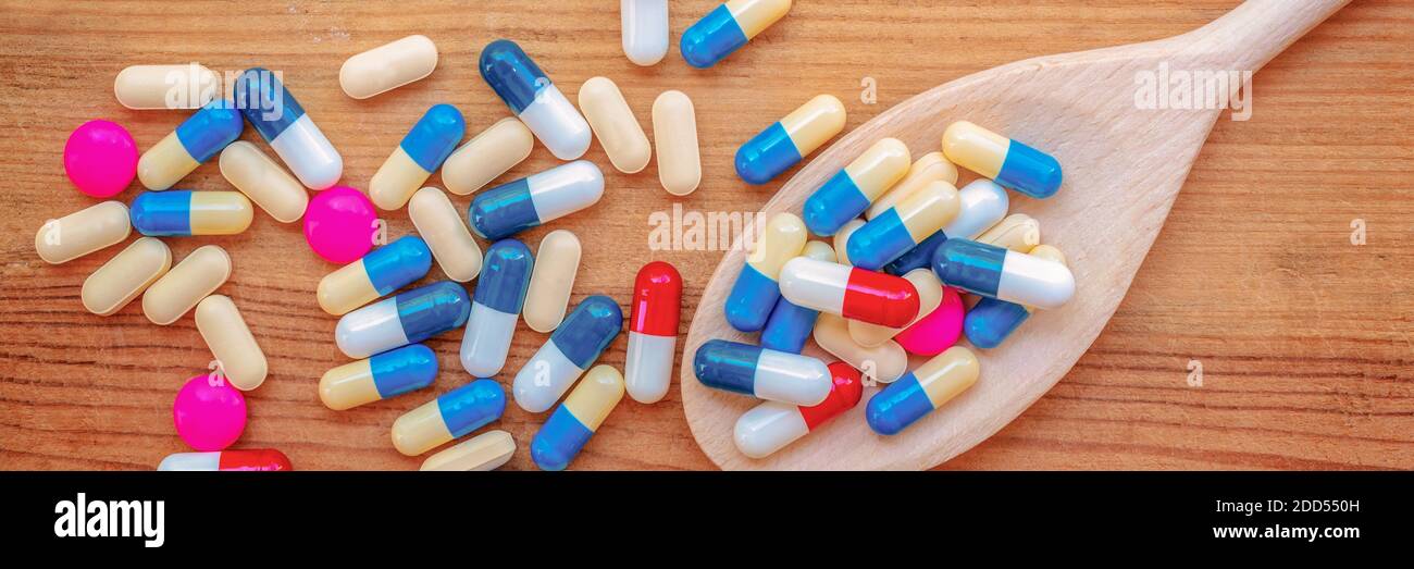 Bunte Pillen und Medikamente in einem hölzernen Kochlöffel, auf Holzplanken Panorama Hintergrund, Gesundheit und Medikamente Konzept Stockfoto