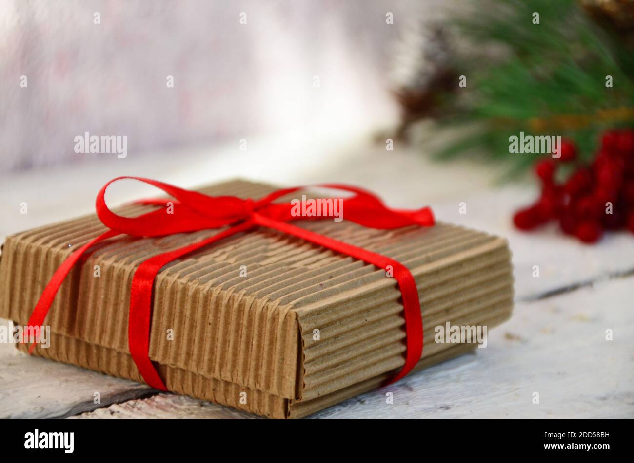 Weihnachts-Geschenkbox mit Dekoration. Box mit einem roten Band gebunden, ein Zweig eines Weihnachtsbaums mit Zapfen, auf einem weißen Holzhintergrund. Stockfoto
