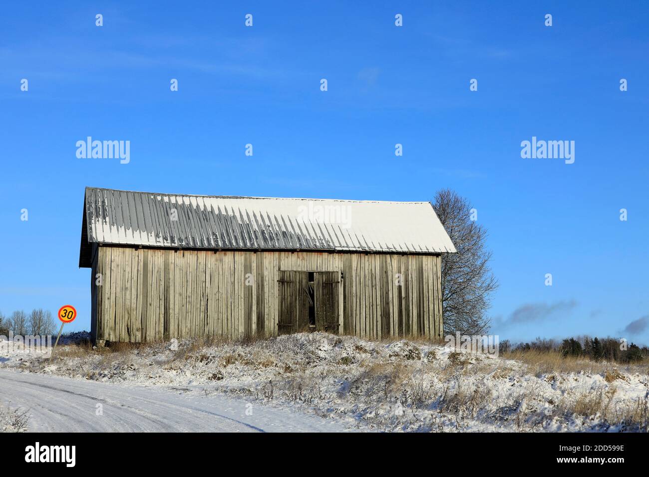 Alte Landscheune unter klarem blauen Himmel durch ländliche Straße im frühen Winter. Stockfoto