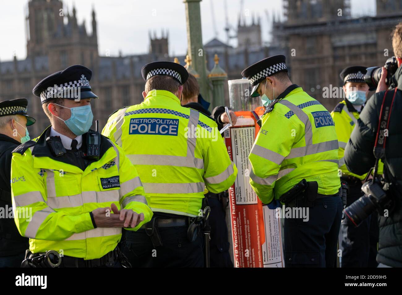 London, Großbritannien. November 2020. Piers Corbyn (Bruder des ehemaligen Labour-Führers Jeremy Corbyn) führte einen kleinen Anti-vax-Anti-Maskenprotest an und verteilte Maskenausnahmemarken an Passanten und die Medien. Er wurde von einem Mann begleitet, der eine riesige Spritze trug, der von der Polizei auf der Westminster Bridge befragt wurde. Kredit: Ian Davidson/Alamy Live Nachrichten Stockfoto