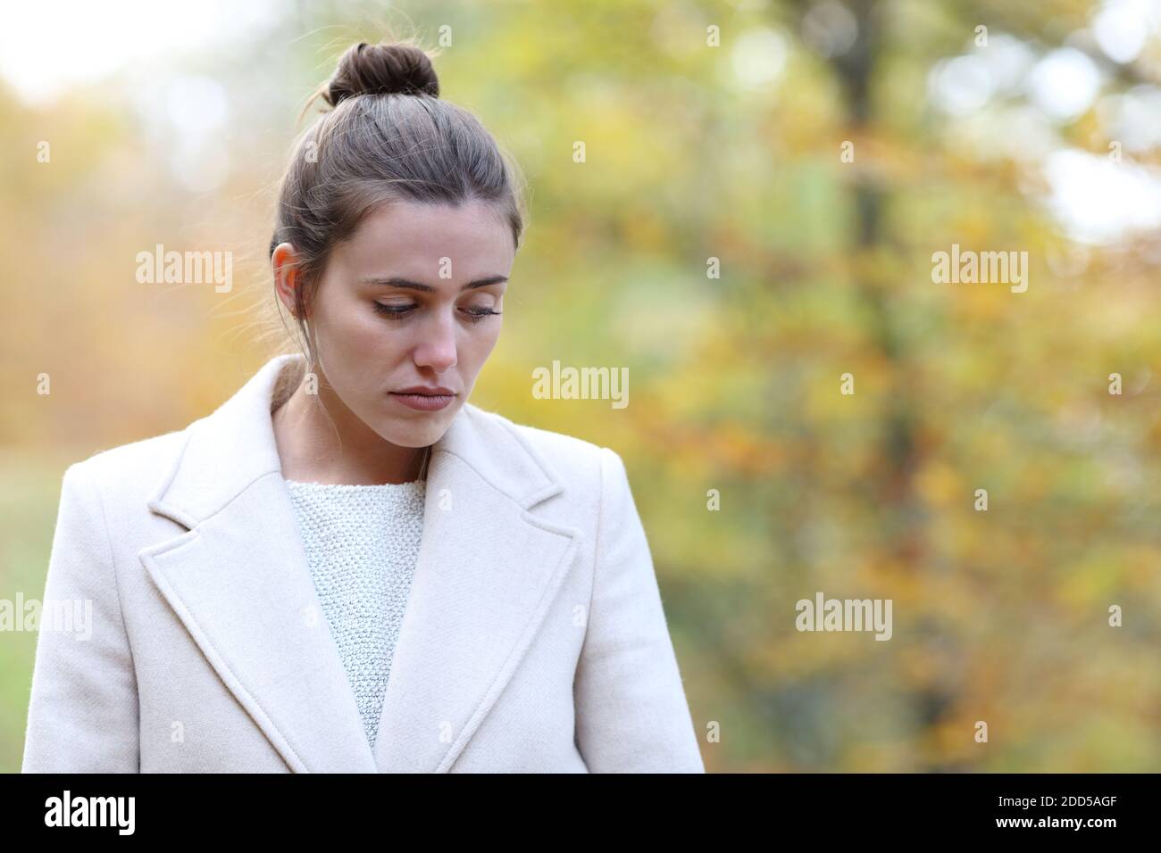 Traurige Frau, die alleine in einem Park hinunterschaut Winter Stockfoto