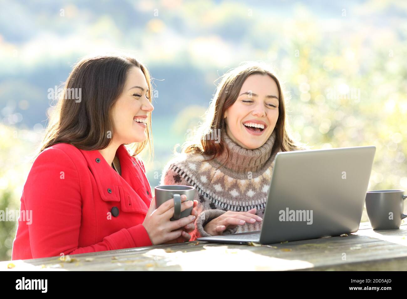 Zwei glückliche Freunde, die im Winter beim Sitzen auf einem Notebook lachen In den Bergen Stockfoto