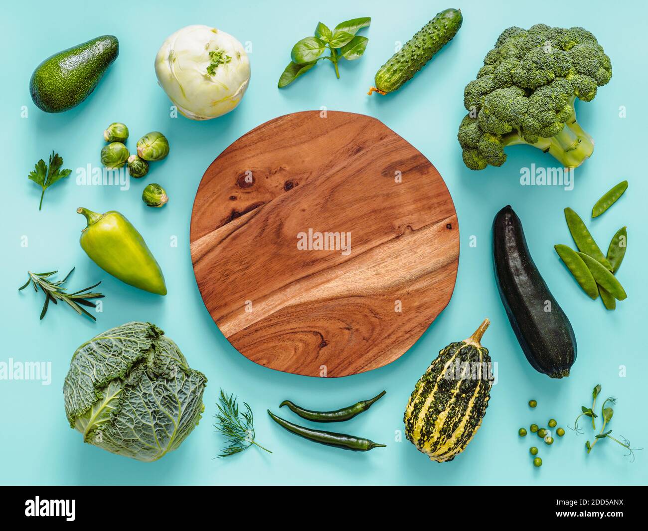 Flach legen mit grünem Gemüse auf blauem Hintergrund, mit Kreis Holzschale in der Mitte. Grüne Erbsen, Zucchini, Avocado, Bohnenschote, Kürbis, Brokkoli, rosenkohl, Rosmarin, Microgreens. Speicherplatz kopieren Stockfoto
